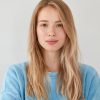 Close up shot of pleasant looking serious blonde Caucasian female with long hair, wears blue casual sweater, looks directly into camera, isolated over white background. People, lifestyle, beauty